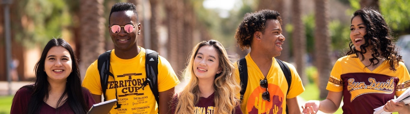 A group of students are on the famous palm walk. They are all wearing ASU gear and are smiling