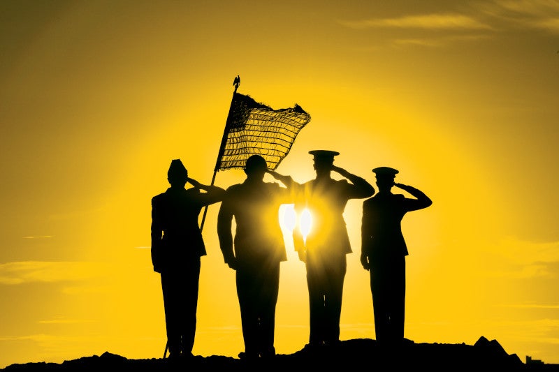 Service members with American flag salute in front of a sunset