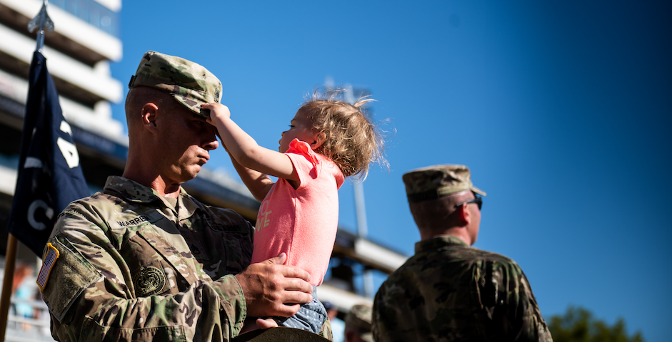 Two military servicemen, one holding a young child wearing a pink shirt