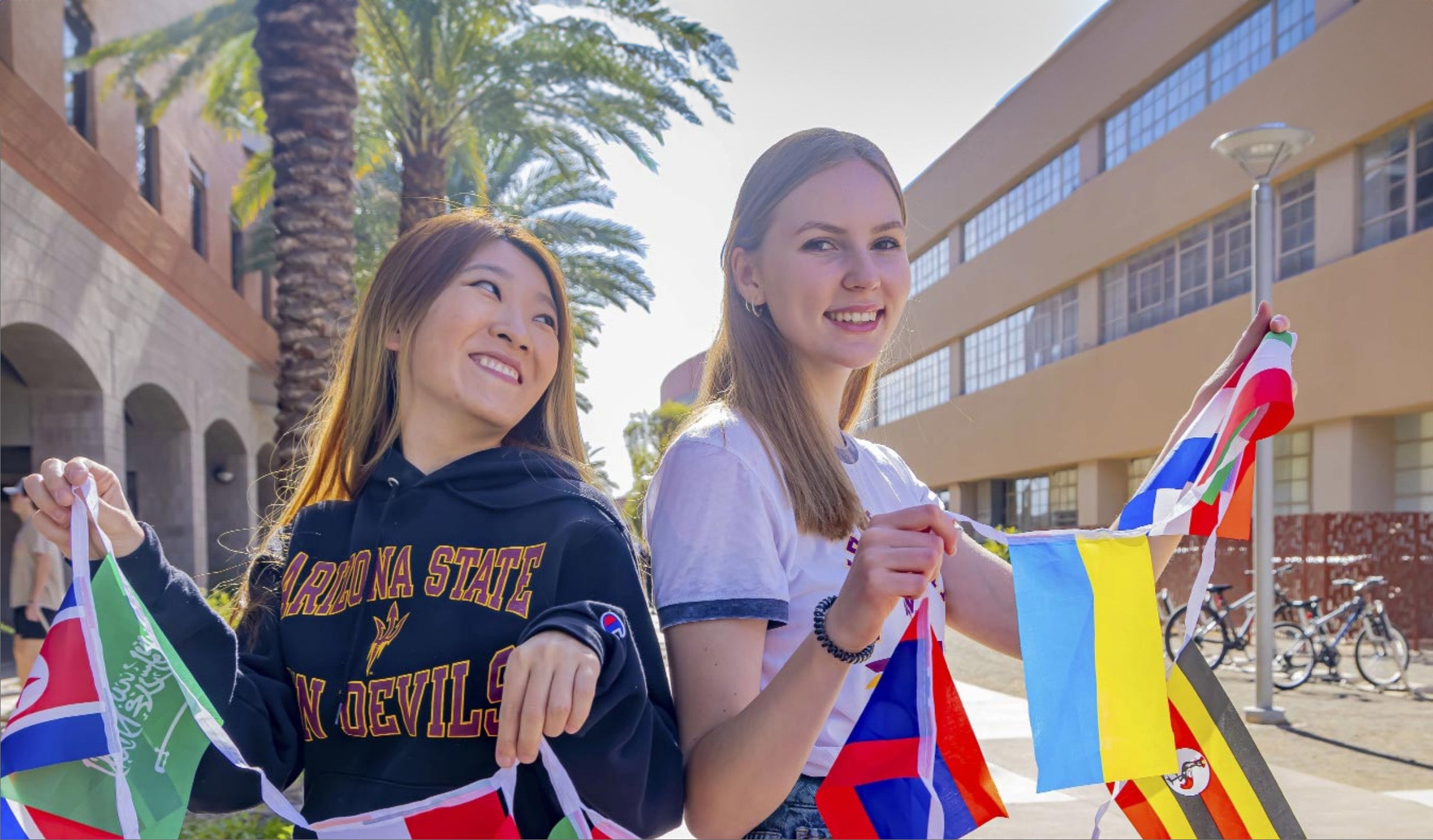 Two women holding a striong of international flags on the A-S-U campus