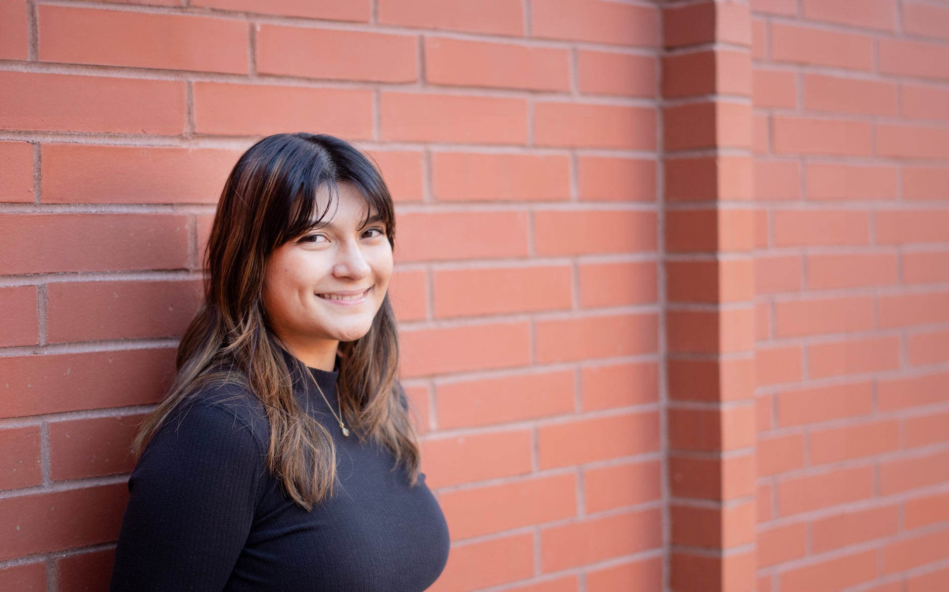 Samantha Delgado, smiling and leaning against a red brick wall