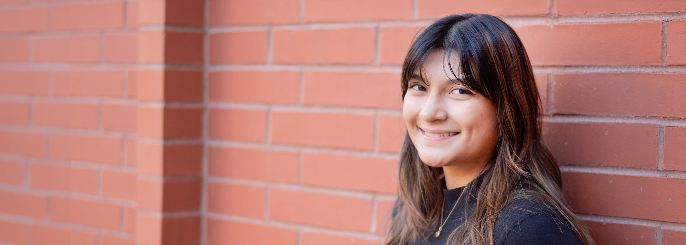 Samantha Delgado smiling and leaning against a brick wall