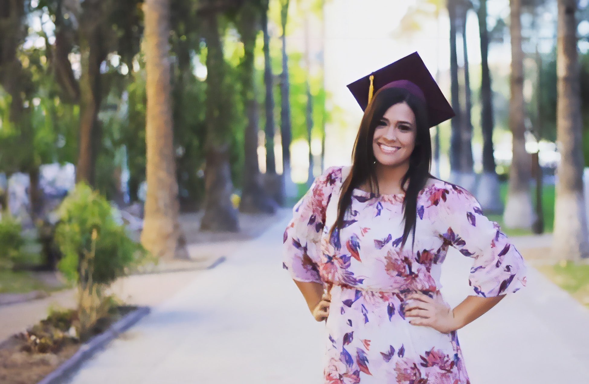 Jennifer Key wearing a graduation cap standing on a paved path with trees in the background