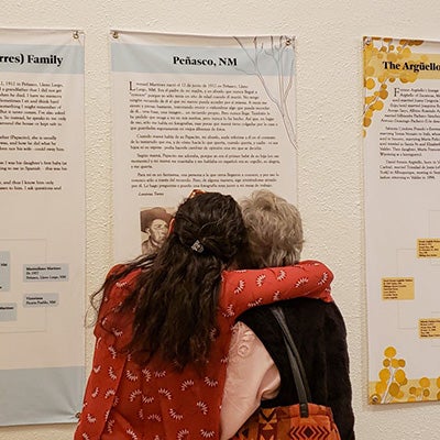 Two women hugging and looking at a poster filled with text hanging on the wall