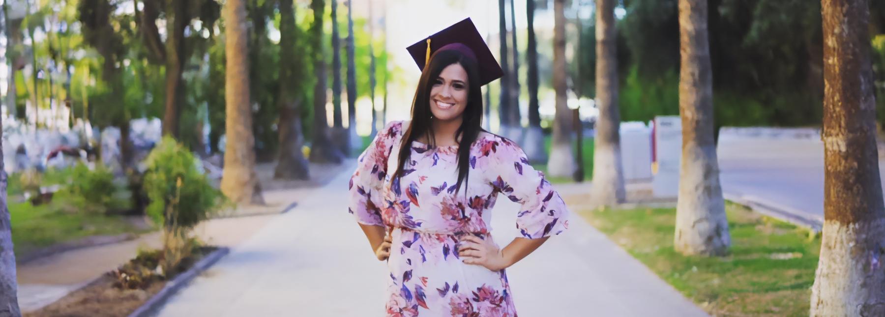 Jennifer Key wearing a graduation cap standing on a paved path with trees in the background
