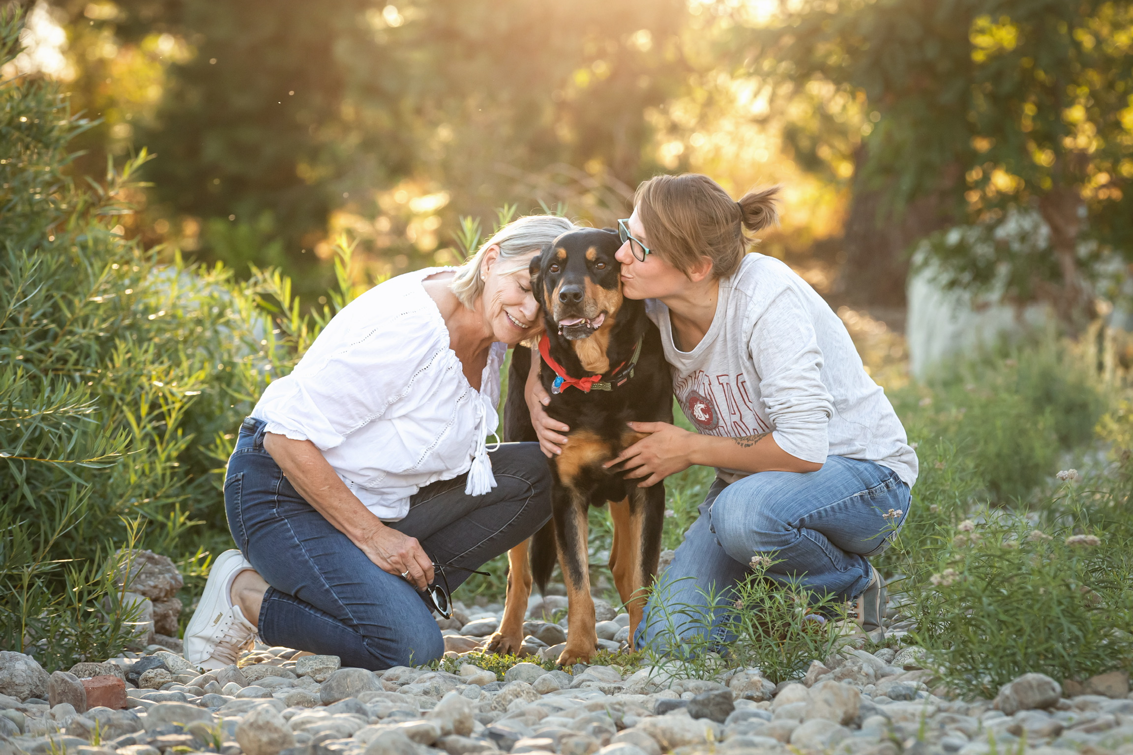 Max is sitting in a field. He is getting snuggled by his two of his family members. One on each side of him.