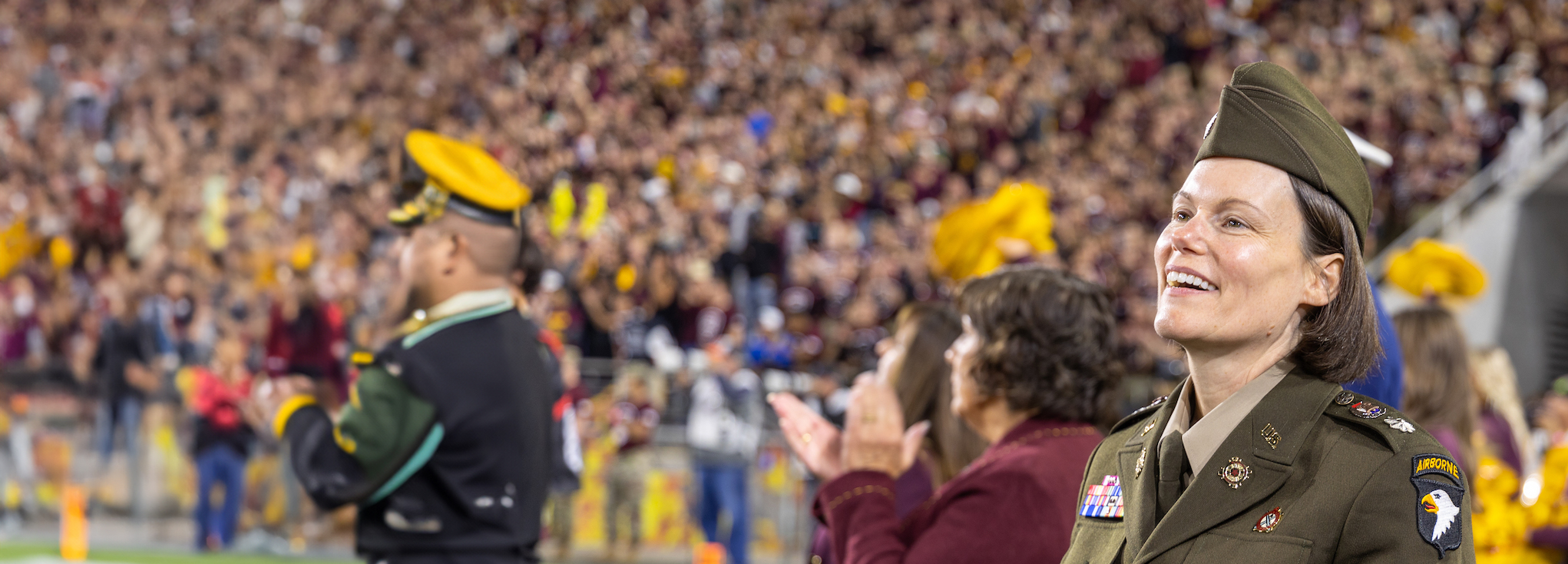 Military memeber in uniform standing in front of a crowd at a football game