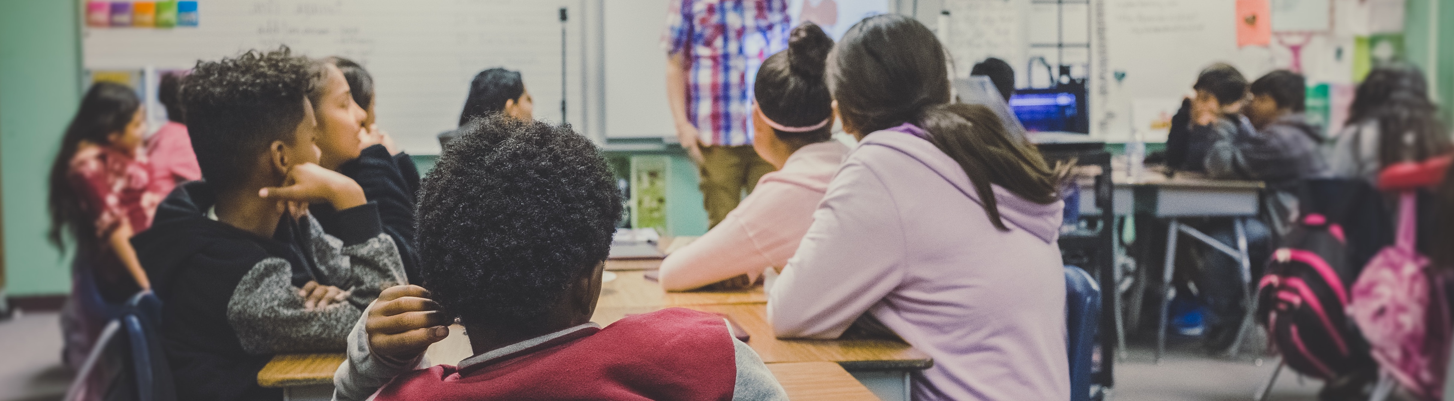 Classroom full of children with someone speaking at the front of the room
