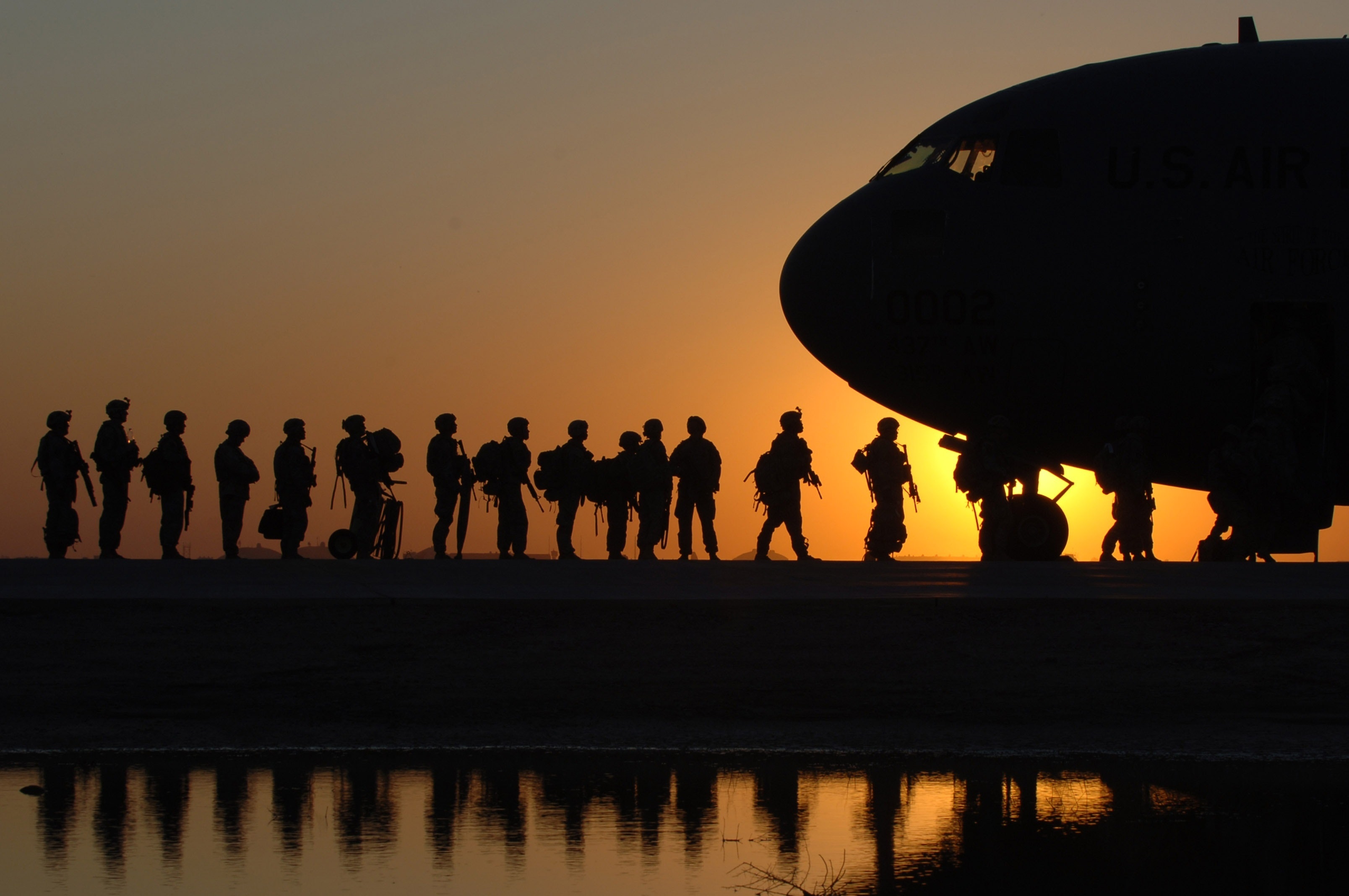 soldier boarding and airplanme behind a sunset