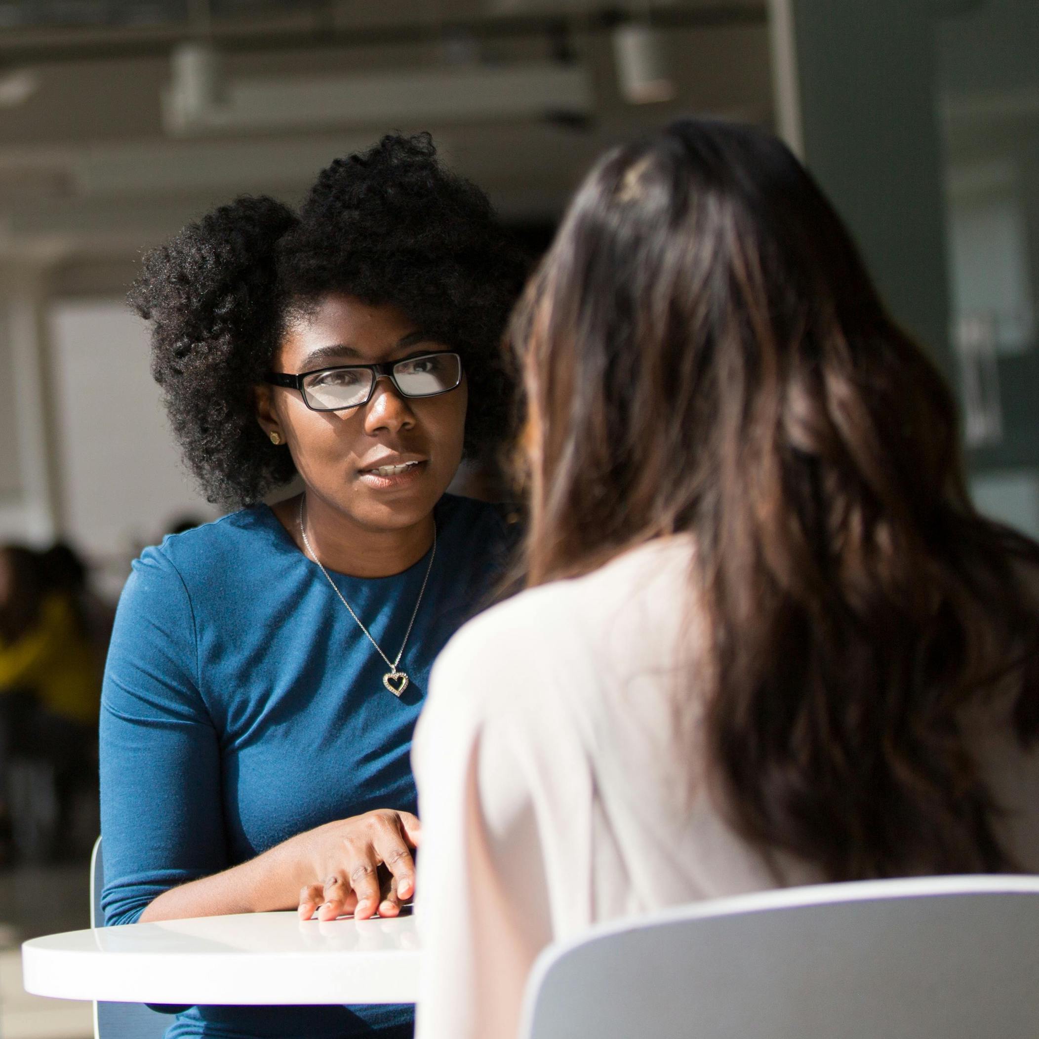 Two women speaking, one with their back turned and the other with a concerned look on her face