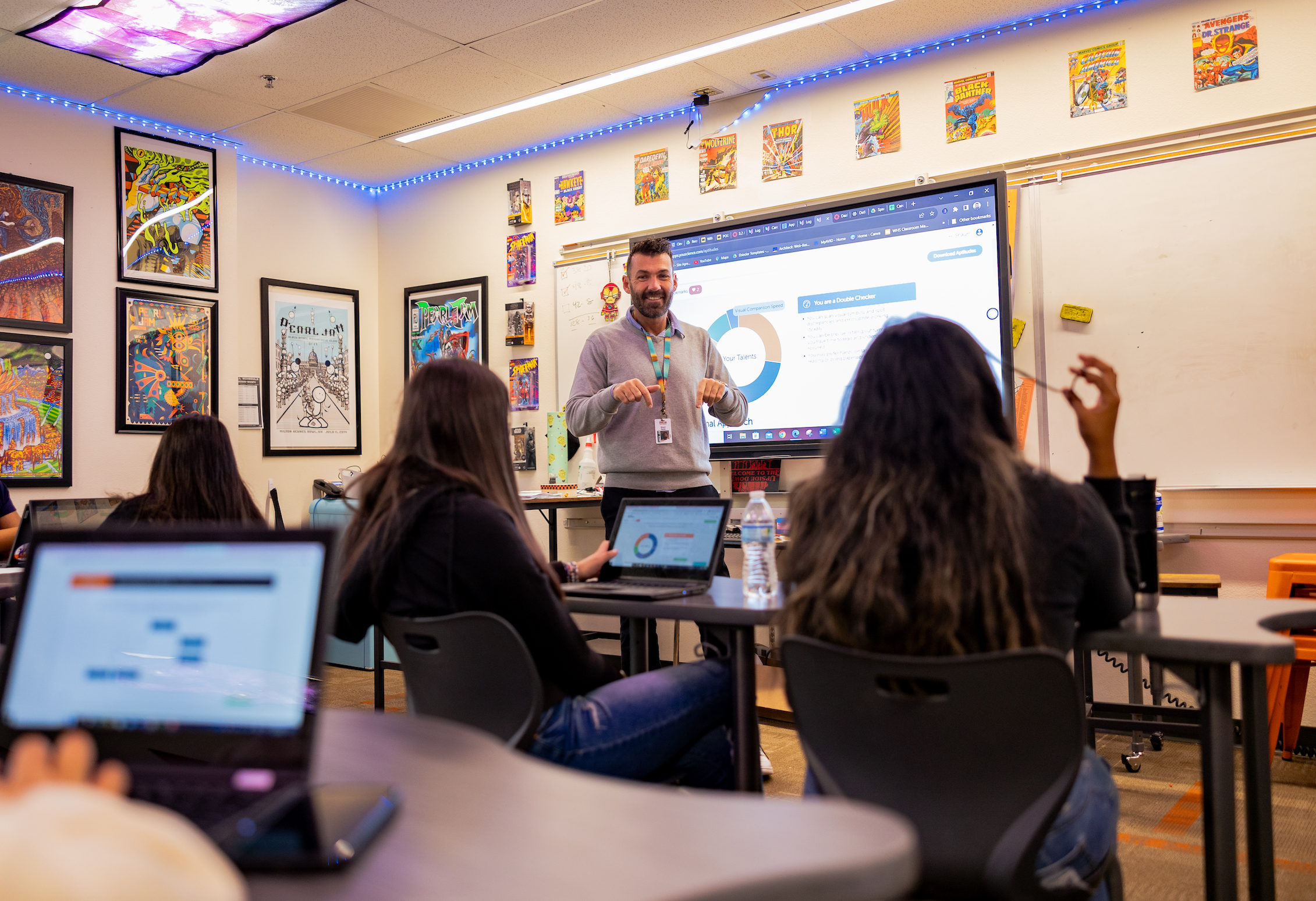 Classroom full of students with an instructor at the front of the room. The room is covered in comic book covers.