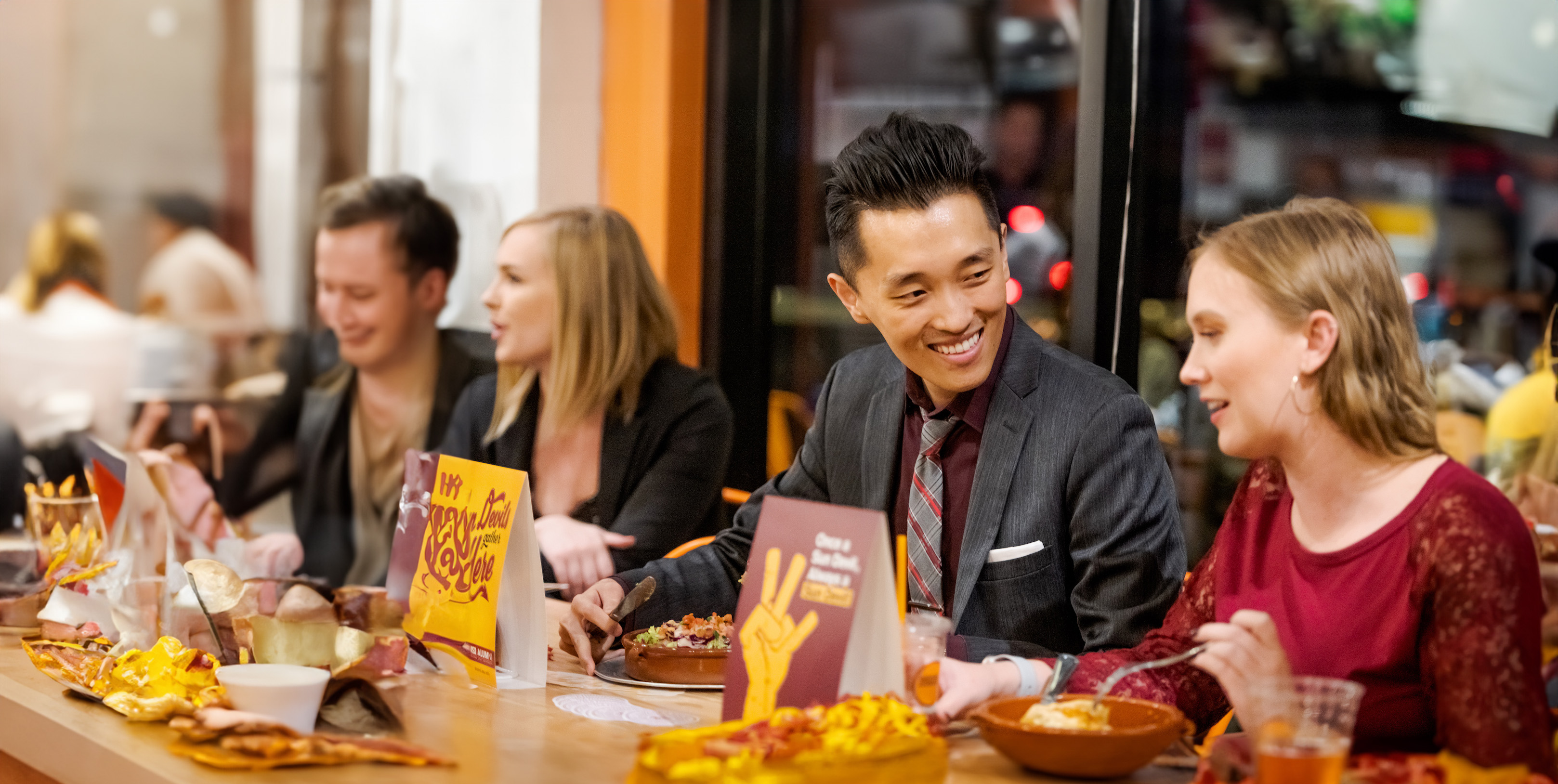 A man and woman sitting at a table enjoying food and talking at an A-S-U branded networking event