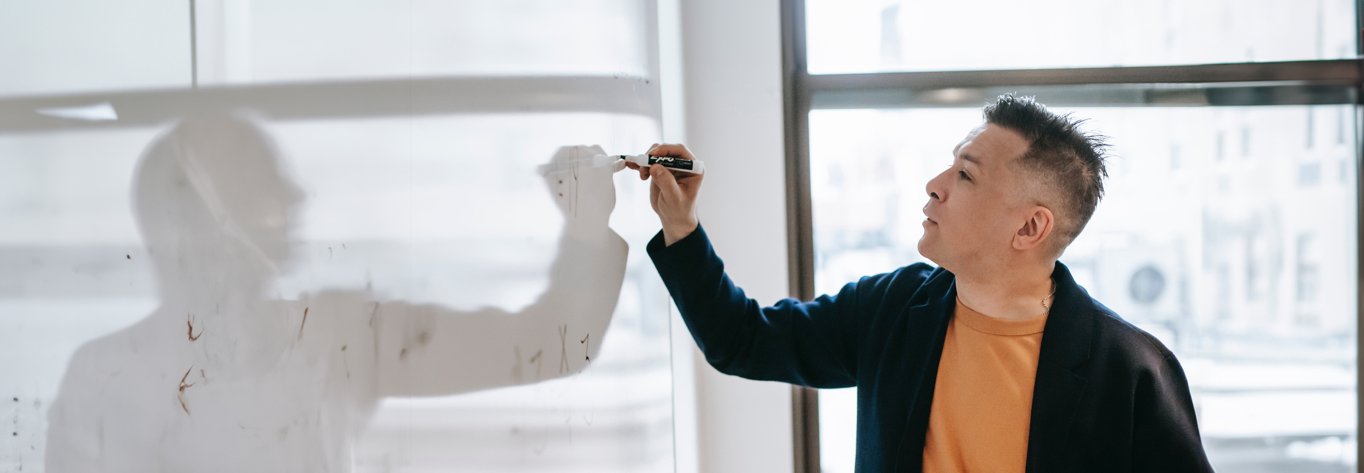 Man writing on a whiteboard in front of a bright, sunny window