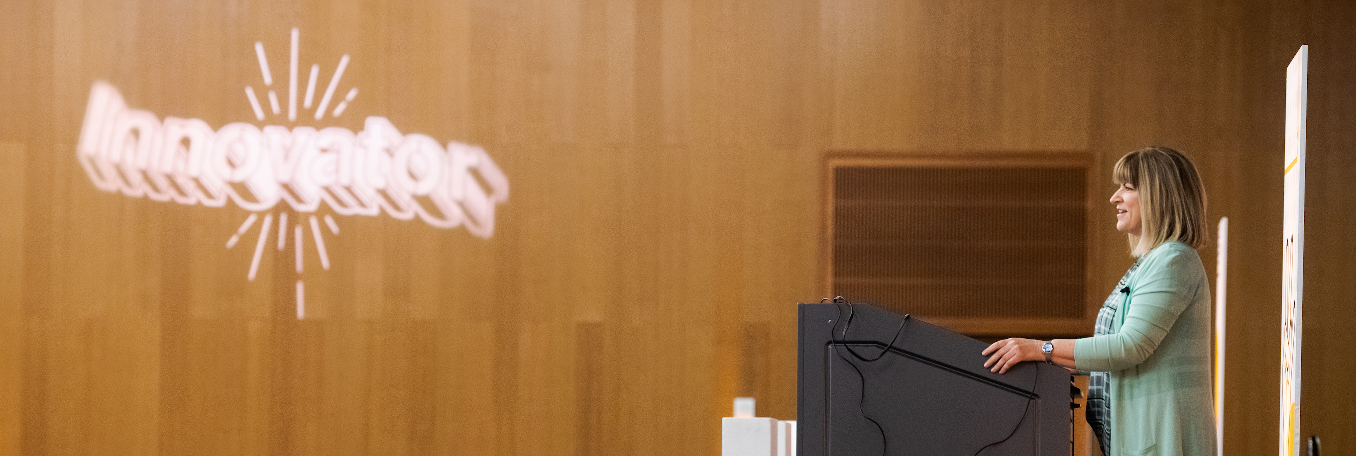 Woman standing at a podium in a wood-paneled room.