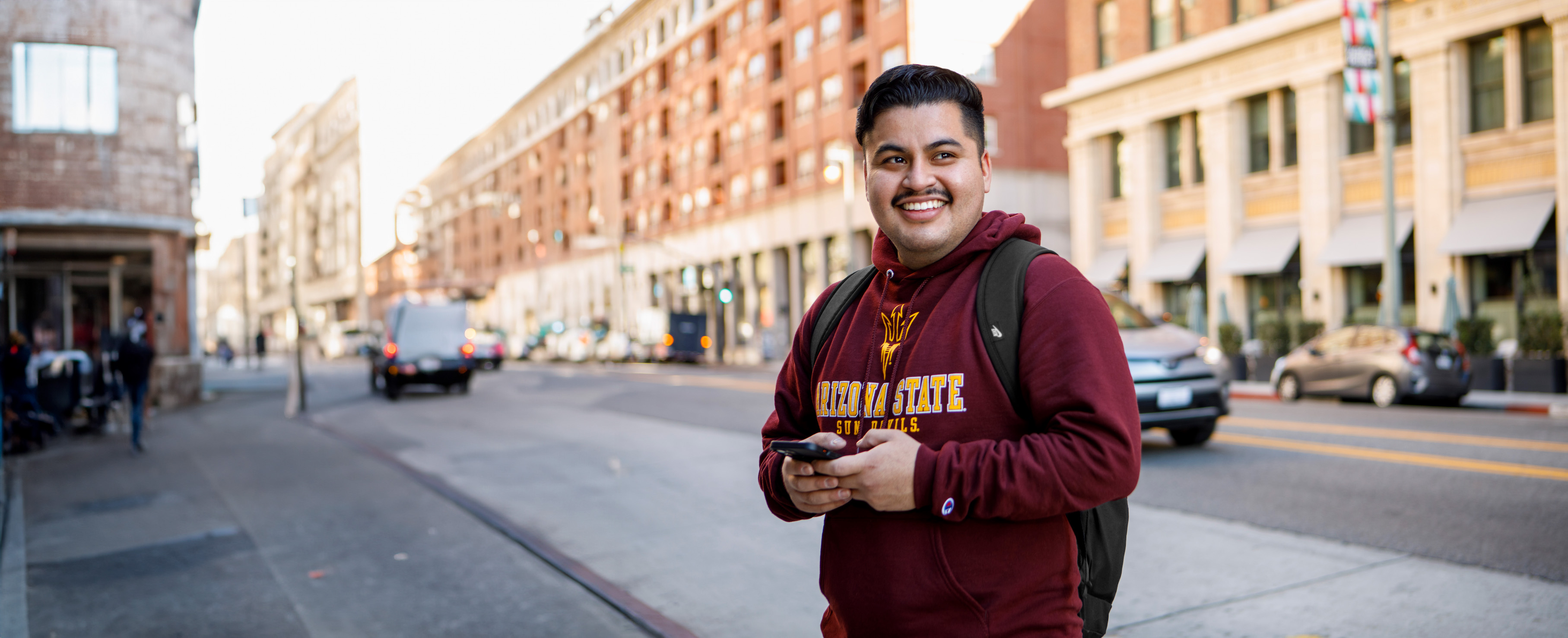 Man wearing A-S-U sweat shirt, standing in an urban environment dense with buildings