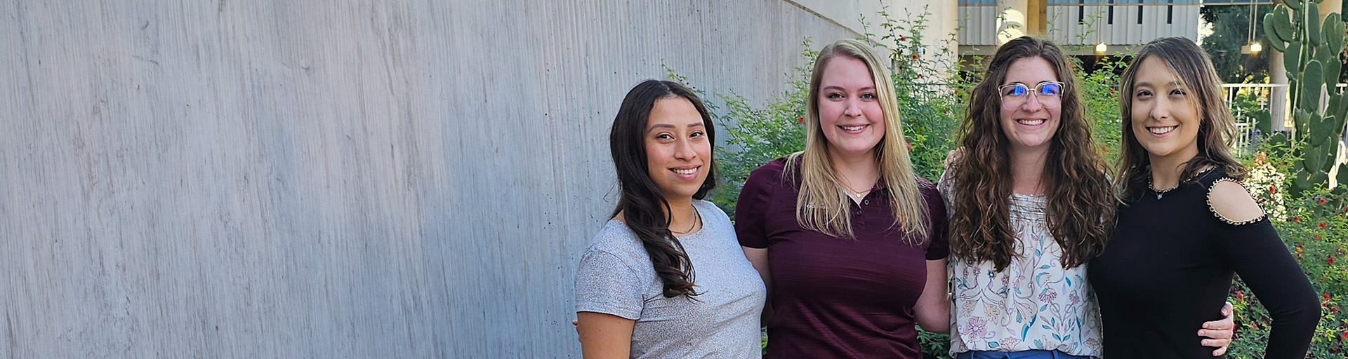 Four School of Counseling and Counseling Psychology staff members standing side by side outdoors, with a concrete wall and garden in the background.