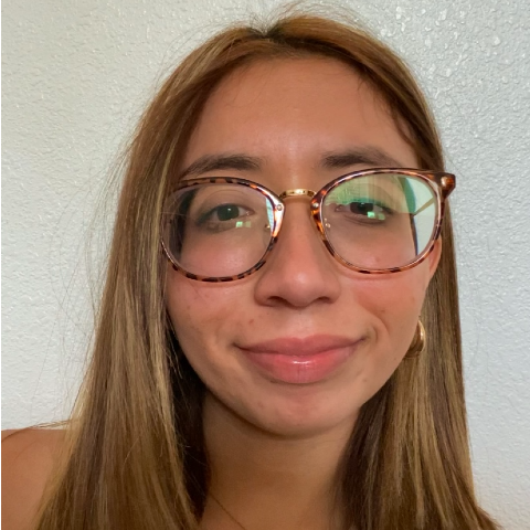 Portrait of a young woman with long light brown hair, wearing tortoise shell glasses. 