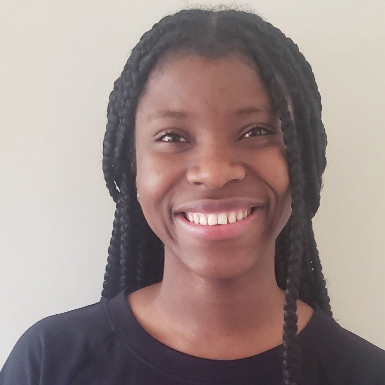 Mary Suku, a young woman with long braids is smiling.